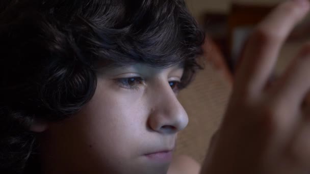Χαριτωμένο έφηβο αγόρι στο δωμάτιό του το βράδυ, ξαπλωμένος στο κρεβάτι χρησιμοποιώντας ένα smartphone. διαβάζει το κείμενο στο τηλέφωνό του. τα μάτια κλείνω 4k. — Αρχείο Βίντεο