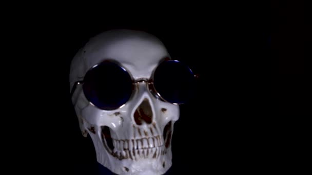 Totenkopf mit runder Sonnenbrille auf schwarzem Hintergrund. Nahaufnahme. 4k, Dolly Shot, Entschärfung, Unschärfe. — Stockvideo