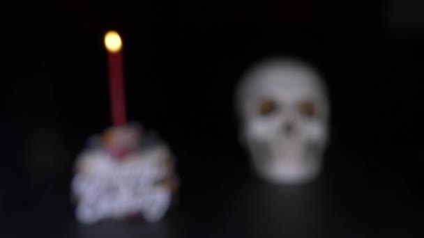 Cake and skull in a festive cap on a black background. 4k, dolly shot, defocusing, blur. — Stock Video