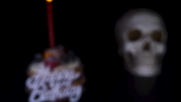 Taart en de schedel in een feestelijke dop op een zwarte achtergrond. 4k, dolly schot, defocusing, vervagen. — Stockvideo