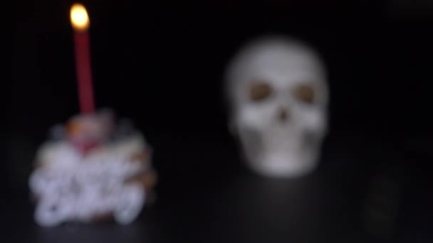 Торт і череп у святковій шапці на чорному тлі. 4k, ляльковий постріл, дефокусування, розмивання . — стокове відео