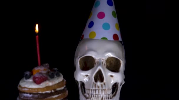 Pastel y el cráneo en una gorra festiva sobre un fondo negro. 4k, dolly shot, desenfoque, desenfoque . — Vídeos de Stock
