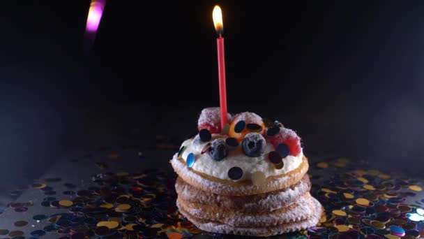 假日, 庆祝和党概念-生日蛋糕与一个燃烧的蜡烛在黑色背景, 五彩纸屑。聚会用的五彩纸屑。4k. 慢动作 — 图库视频影像