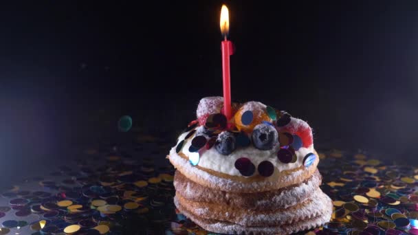 Ünnep, az ünneplés és a fél fogalma - birthday cupcake egy égő gyertya felett a fekete háttér, konfetti. Konfetti a párt. Super slow motion — Stock videók