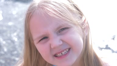 Portre, yakın çekim. Küçük kız kameraya, 4 k, ağır çekim resim arıyorum çocuk deniz kenarında oynarken yüz