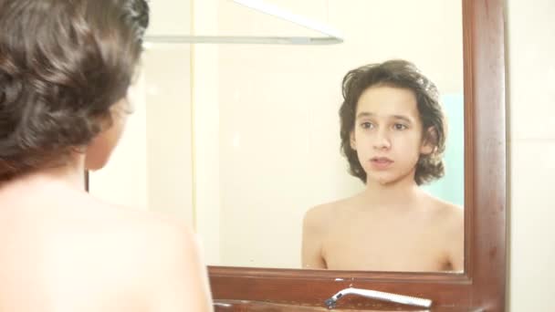 Garçon adolescent se lave le visage devant un miroir. il se regarde dans le miroir et sourit. 4k . — Video