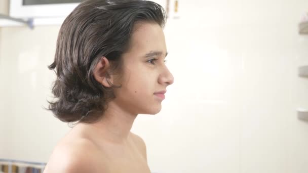 Tiener jongen is het wassen van zijn gezicht in een spiegel. Hij bekijkt zichzelf in de spiegel en glimlacht. 4k. — Stockvideo