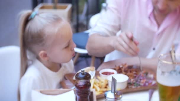 4k, detail. Otec a jeho malá dcera jíst fast food na terase restaurace rychlého občerstvení. — Stock video