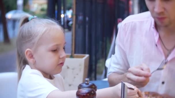 4k, close-up. Dad and his little daughter eat fast food on the terrace of a fast food restaurant. — Stock Video