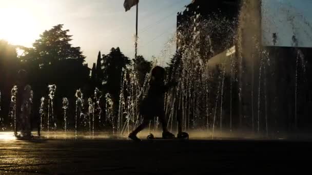 Sylwetki dzieci grać w fontannie siedzib w letni dzień. 4k. — Wideo stockowe