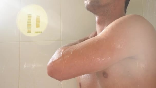 Joven guapo tomando una ducha en el baño. Está iluminado por los rayos del sol desde la ventana. 4k, cámara lenta . — Vídeo de stock