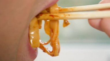 yakın çekim. profil erkek dudaklarında. adam kırmızı soslu spagetti yemek çubukları, yiyor. 4k, ağır çekim.