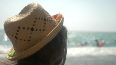 4k, yakın çekim. Hasır şapkalı kız denizin dalgaları görünüyor. Arkadan görünüm. Ağır çekim