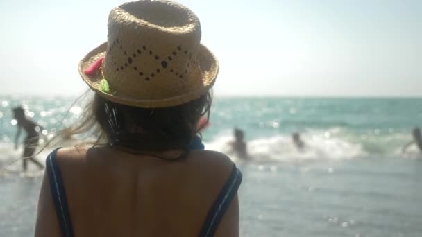 4k, yakın çekim. Hasır şapkalı kız denizin dalgaları görünüyor. Arkadan görünüm. Ağır çekim — Stok video
