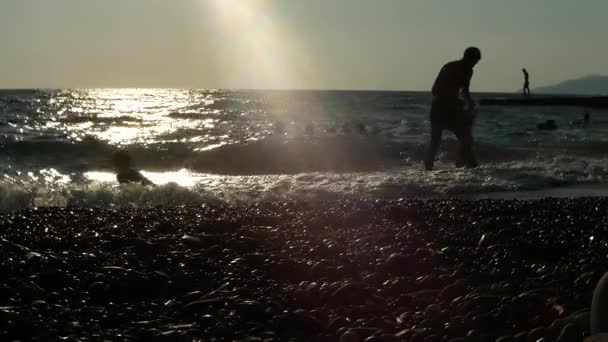 Силуэт неузнаваемости счастливых людей, играющих на пляже на закате. — стоковое видео