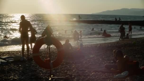 Lifebuoy en una playa pública. siluetas de la gente. bronceado, natación, turismo, descanso y relajación — Vídeos de Stock