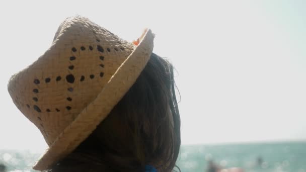 4k, gros plan. la jeune fille au chapeau de paille regarde les vagues de la mer. vue arrière. Mouvement lent — Video