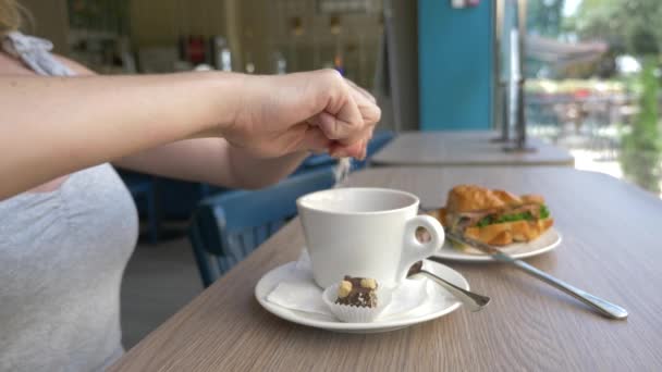 Uma mulher irreconhecível com um belo decote, pequenos-almoços em um café com um sanduíche croissant com carne de porco fervida e beber café. 4k, câmera lenta, close-up . — Vídeo de Stock