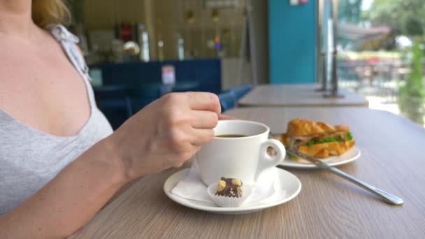 Une femme méconnaissable avec un beau décolleté, des petits déjeuners dans un café avec un croissant sandwich au porc bouilli et boire du café. 4k, ralenti, gros plan . — Video