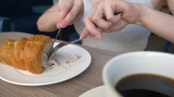 Una mujer irreconocible con un hermoso escote, desayunos en un café con un sándwich de croissant con cerdo hervido y beber café. 4k, cámara lenta, primer plano . — Vídeos de Stock