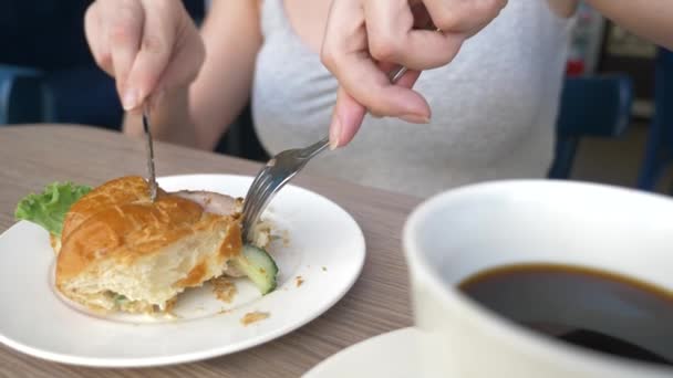 Seorang wanita yang tidak dikenal dengan kalung yang indah, sarapan di sebuah kafe dengan roti lapis croissant dengan daging babi rebus dan minum kopi. 4k, slow-motion, close-up . — Stok Video