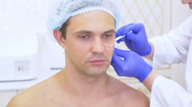 Güzellik uzmanı Doktor elinde bir kalem ile adam yüzünde işaretler yapar. kontur yüz plastik. 4 k. ağır çekim