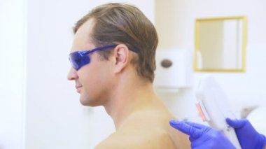 Mens lazer epilasyon. Doktor mavi eldiven omuz ve boyun yakışıklı bir genç adam, saç kaldırır. 4k, yakın çekim. Ağır çekim