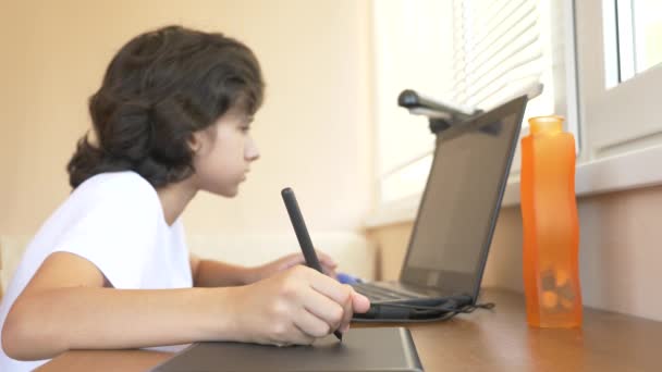 Knappe jongen van de moderne tiener werken op een grafisch tablet. Hij kijkt naar het scherm van de laptop. 4k, slow-motion — Stockvideo