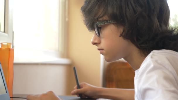 Bonito menino moderno adolescente trabalhando em um tablet gráfico. Ele olha para o ecrã do portátil. 4k, câmera lenta — Vídeo de Stock