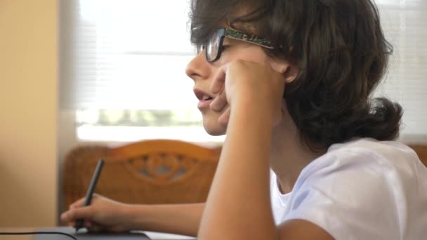 Bonito menino moderno adolescente trabalhando em um tablet gráfico. Ele olha para o ecrã do portátil. 4k, câmera lenta — Vídeo de Stock