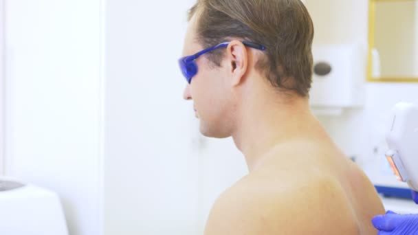 Мужская лазерная эпиляция. Доктор в синих перчатках снимает волосы с плеч и шеи красивого молодого человека. 4К, крупный план. Медленное движение — стоковое видео