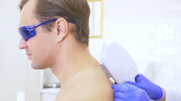 Pánské laserové epilace. lékař v modré rukavice odstraní vlasy z ramen a krku pohledný mladý muž. 4k, detail. Zpomalený pohyb — Stock video