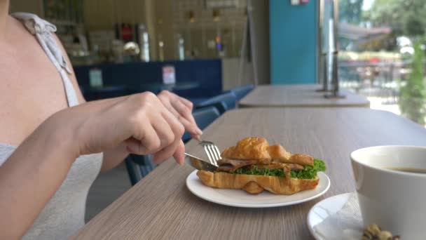 Eine unkenntliche Frau mit schönem Dekolleté frühstückt in einem Café mit einem Croissant-Sandwich mit gekochtem Schweinefleisch und trinkt Kaffee. 4k, Zeitlupe, Nahaufnahme. — Stockvideo