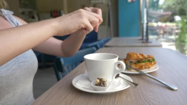 Una mujer irreconocible con un hermoso escote, desayunos en un café con un sándwich de croissant con cerdo hervido y beber café. 4k, cámara lenta, primer plano . — Vídeos de Stock