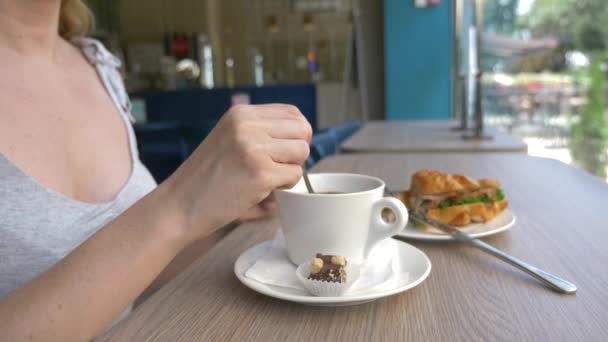 An unrecognizable woman with a beautiful neckline, breakfasts in a cafe with a croissant sandwich with boiled pork and drinking coffee. 4k, slow-motion, close-up. — Stock Video