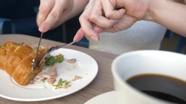 Una mujer irreconocible con un hermoso escote, desayunos en un café con un sándwich de croissant con cerdo hervido y beber café. 4k, cámara lenta, primer plano . — Vídeos de Stock