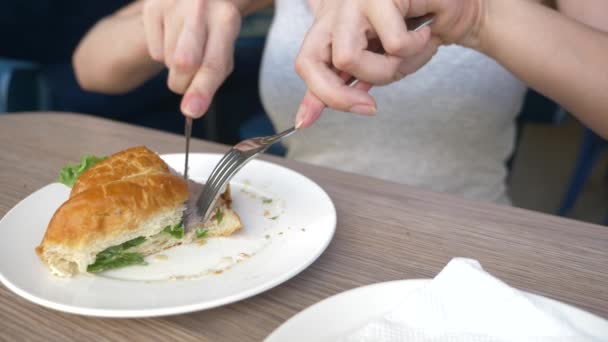 Une femme méconnaissable avec un beau décolleté, des petits déjeuners dans un café avec un croissant sandwich au porc bouilli et boire du café. 4k, ralenti, gros plan . — Video