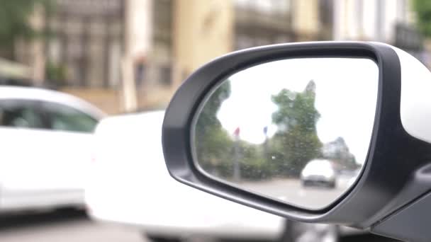 Espelho retrovisor do carro com vestígios de chuva. uma reflexão turva no espelho retrovisor de um carro parado à beira da estrada, passando por carros e passando por pedestres. 4k, câmera lenta — Vídeo de Stock