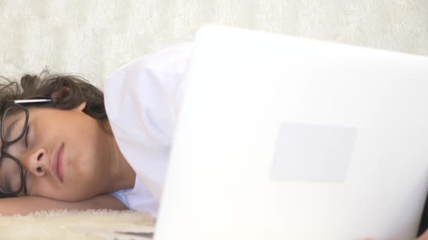 Милый подросток в очках спит на диване рядом с ноутбуком. 4k — стоковое видео