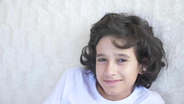 Schattige curly-haired jongen de tiener kijkt naar de camera lachen en maakt een grappige gelaatsuitdrukking. 4 k, slow motion, close-up — Stockvideo