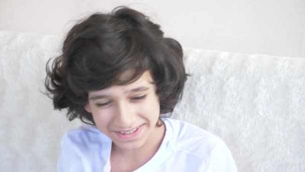 Ładny chłopak kręconych włosach nastolatek patrzy na aparat, śmiejąc się i sprawia, że zabawny wyraz twarzy. 4 k, zwolnionym tempie, zbliżenie — Wideo stockowe