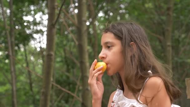 Linda niña morena, comiendo fruta y hablando. Fondo de la naturaleza. 4k, cámara lenta — Vídeos de Stock