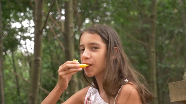 Söt liten brunett av flicka, äta frukt och prata. Natur bakgrund. 4k, Slowmotion — Stockvideo