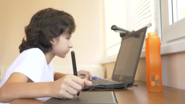 Bonito menino moderno adolescente trabalhando em um tablet gráfico. Ele olha para o ecrã do portátil. 4k, câmera lenta — Vídeo de Stock