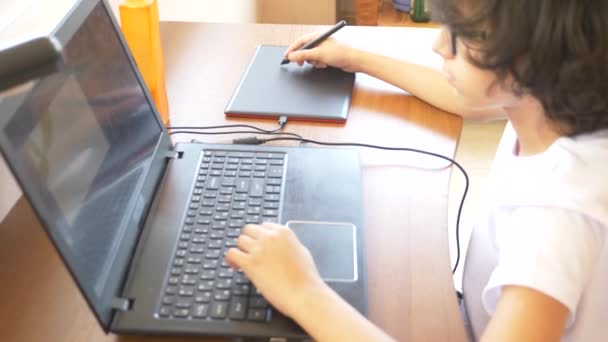 モダンな美少年ティーンエイ ジャー グラフィック タブレットに取り組んでいます。彼はノート パソコンの画面を見てください。4 k、スローモーション — ストック動画