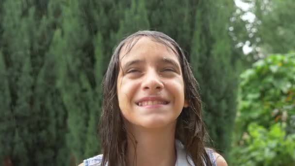 Close-up. retrato de uma jovem olhando para a chuva na natureza com o cabelo molhado. a menina se alegra com a chuva torrencial, gotas de água caem em seu rosto. 4K. Movimento lento — Vídeo de Stock