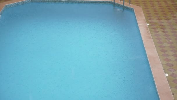 Las gotas de lluvia caen al agua azul. Hermosa superficie de agua de piscina bajo la lluvia. En cámara lenta. 4k — Vídeo de stock