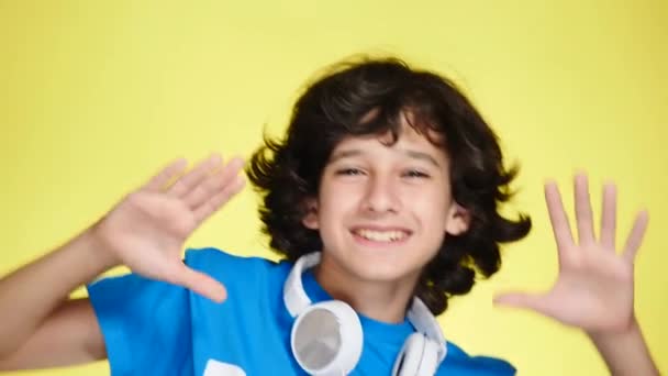 Tiener jongen met hoofdtelefoons en mobiele telefoon luisteren naar muziek op de achtergrond in kleur. Close-up, 4k, slow-motion. — Stockvideo