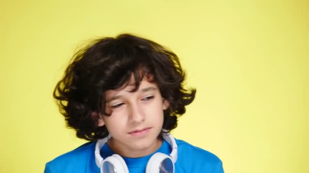 Niño adolescente con auriculares y teléfono móvil escuchando música en el fondo de color. primer plano, 4k, cámara lenta . — Vídeo de stock