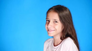 Uzun saçlı sevimli heyecan çekici kız portresi. mavi arka plan üzerinde dururken gülüyor. 4 k, yavaş hareket, yakın çekim